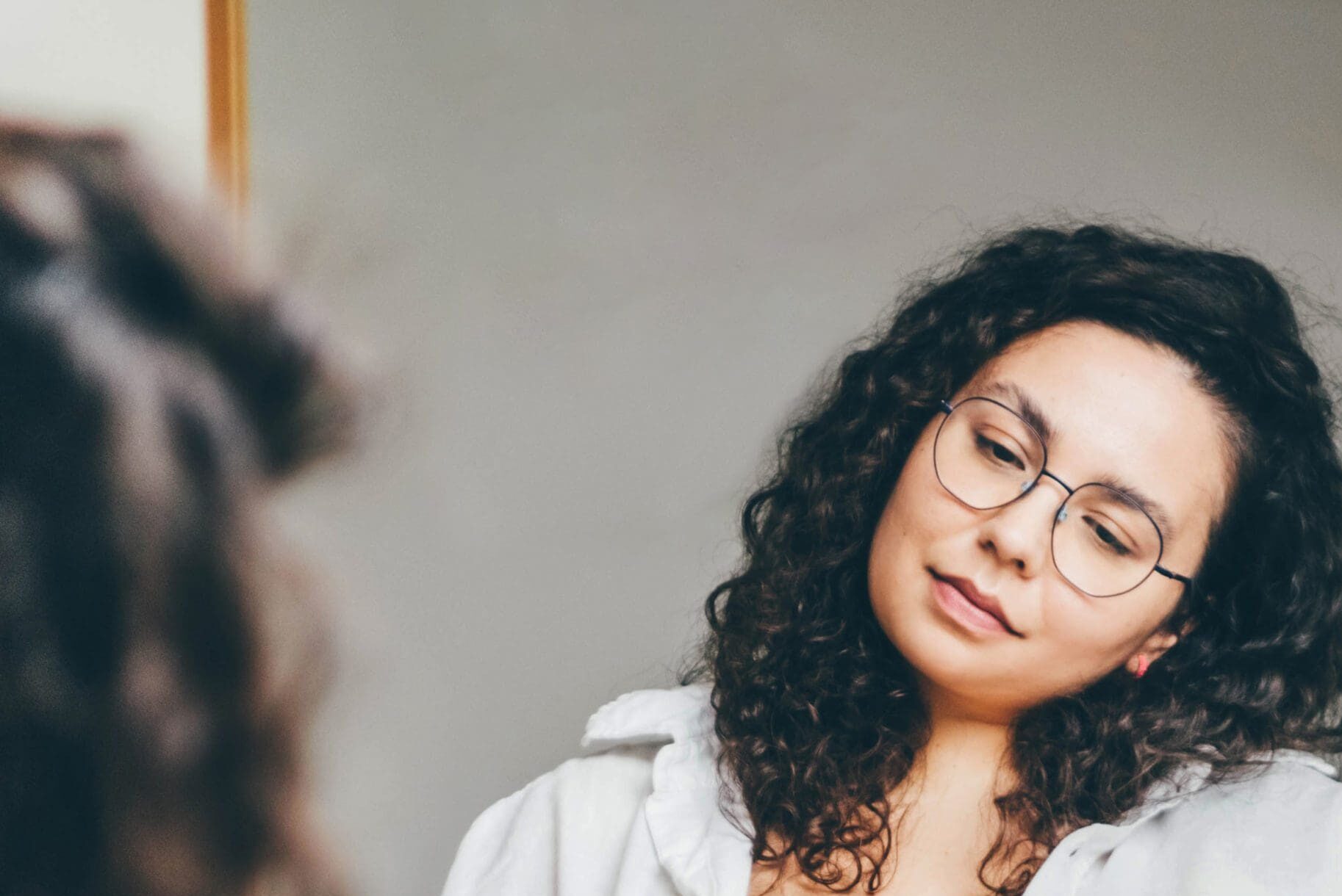 Woman thoughtfully looking at herself in the mirror.