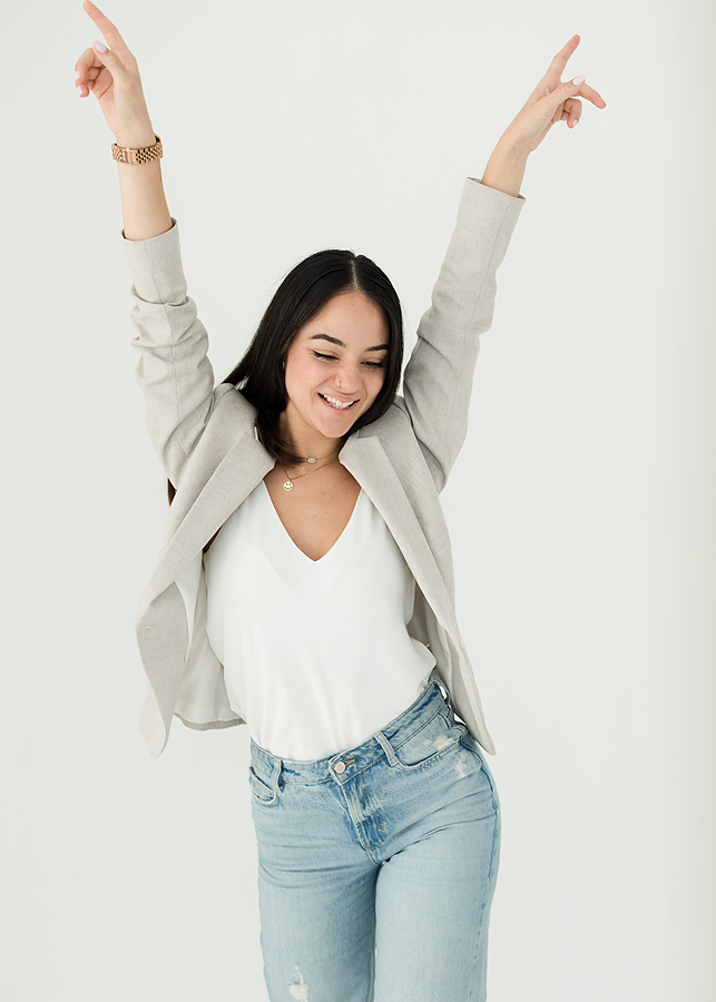 Young woman wearing jeans and blazer dancing with hands in the air